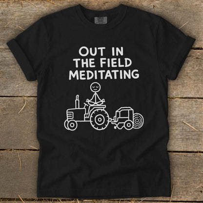 Black t-shirt with "OUT IN THE FIELD MEDITATING" text and a stick figure meditating on a tractor.