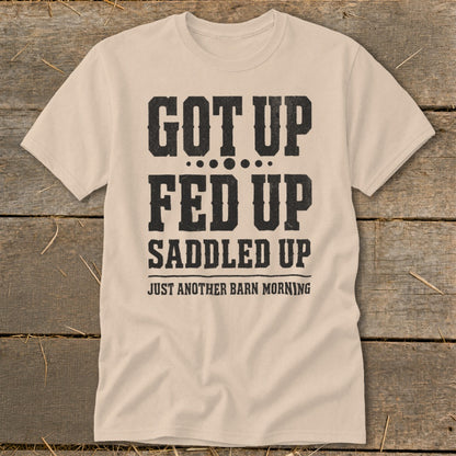 Light beige t-shirt with black text reading "GOT UP FED UP SADDLED UP JUST ANOTHER BARN MORNING".