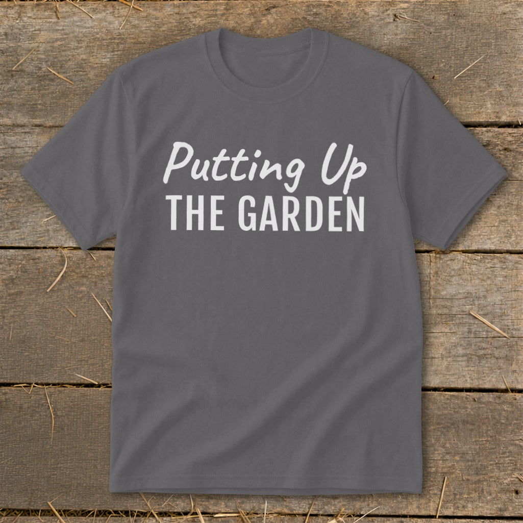 Gray t-shirt with white text "Putting Up THE GARDEN" on a wooden background.
