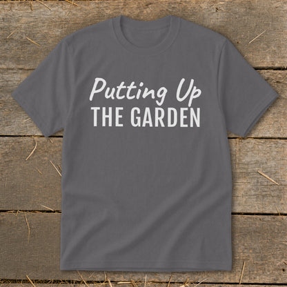 Gray t-shirt with white text "Putting Up THE GARDEN" on a wooden background.