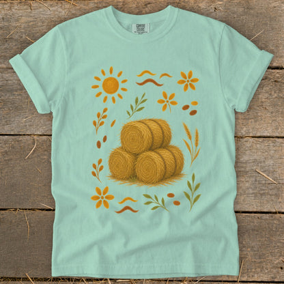 Mint green t-shirt with a stylized autumn harvest graphic featuring hay bales and sun.