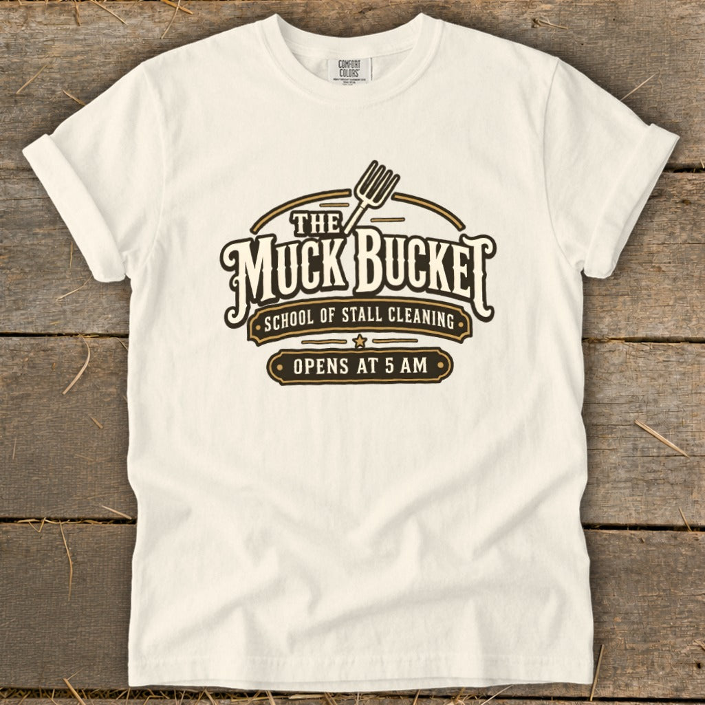 Cream t-shirt with "The Muck Bucket School of Stall Cleaning Opens at 5 AM" graphic.
