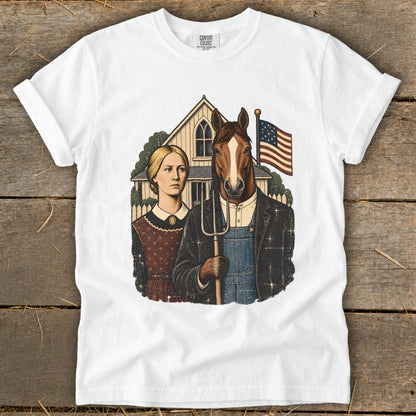 A white short-sleeved t-shirt featuring a graphic parody of American Gothic, showing a woman and a man with a horse head holding a pitchfork.