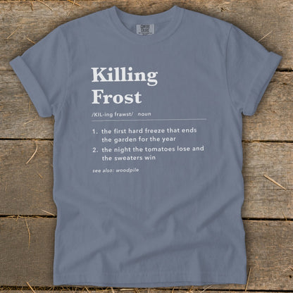A slate blue t-shirt printed with a dictionary definition of Killing Frost lies flat on a wooden surface.
