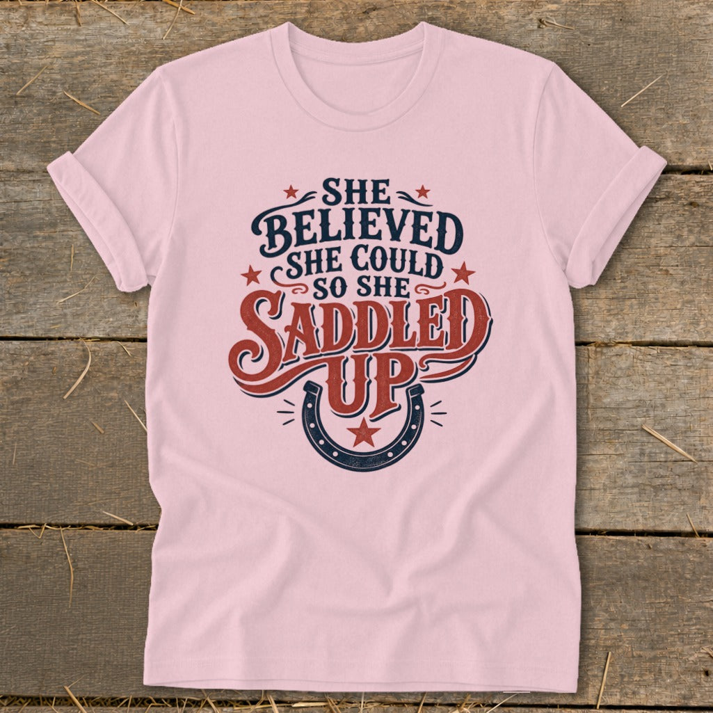 Pink t-shirt with "She believed she could so she saddled up" text and horseshoe graphic.