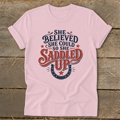 Pink t-shirt with "She believed she could so she saddled up" text and horseshoe graphic.