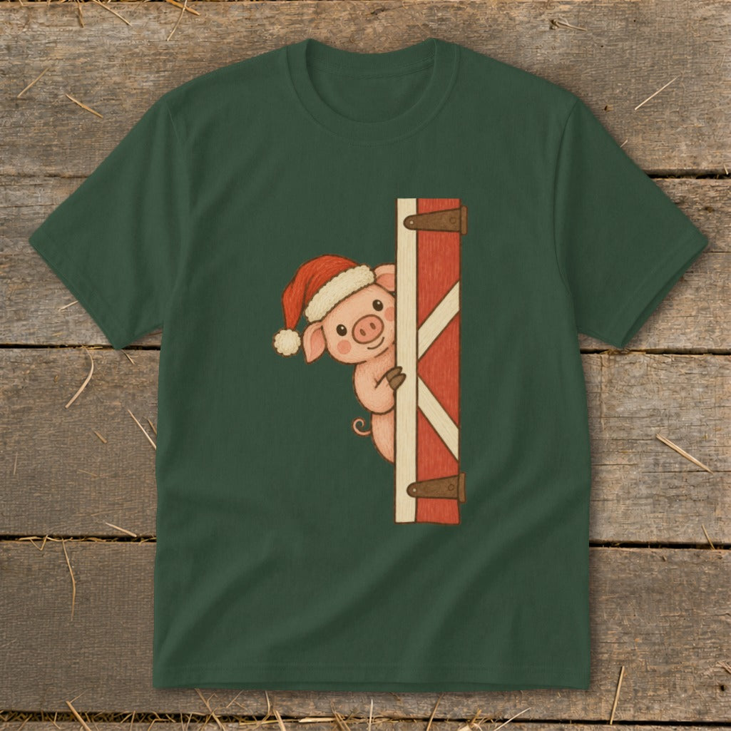 Christmas pig in a Santa hat peeking around a red barn door on a green shirt.