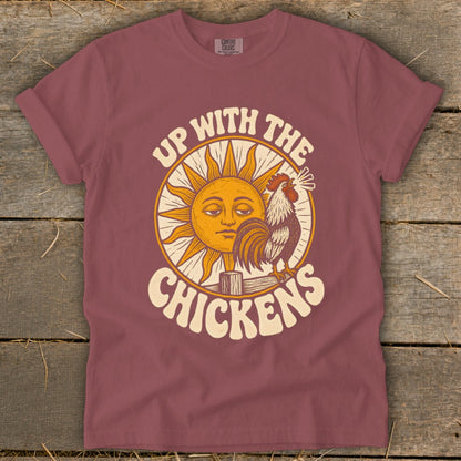 Dusty rose short-sleeve t-shirt with a vintage-style graphic of a rooster, a sun, and the text Up With The Chickens.