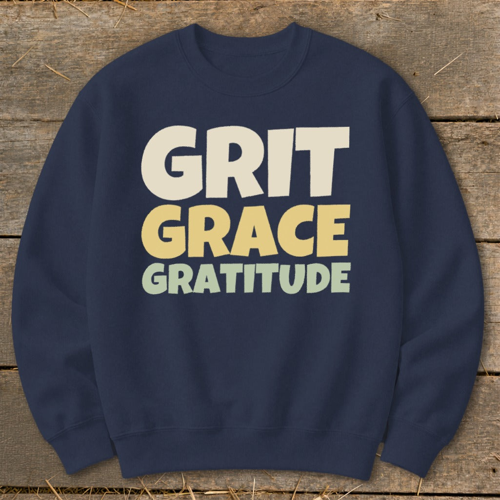 A dark blue crewneck sweatshirt with the words GRIT GRACE GRATITUDE printed across the chest in three different pastel colors.