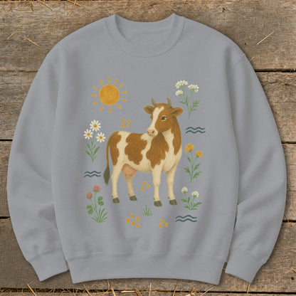 Light blue sweatshirt with a brown and white cow, sun, and wildflowers illustration.