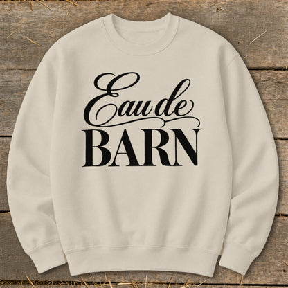 Cream sweatshirt with black text "Eau de BARN" on wooden background.
