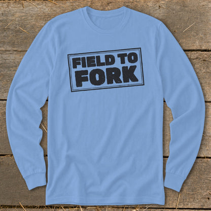 Light blue long-sleeve t-shirt with a distressed black framed graphic reading FIELD TO FORK on a wooden background.