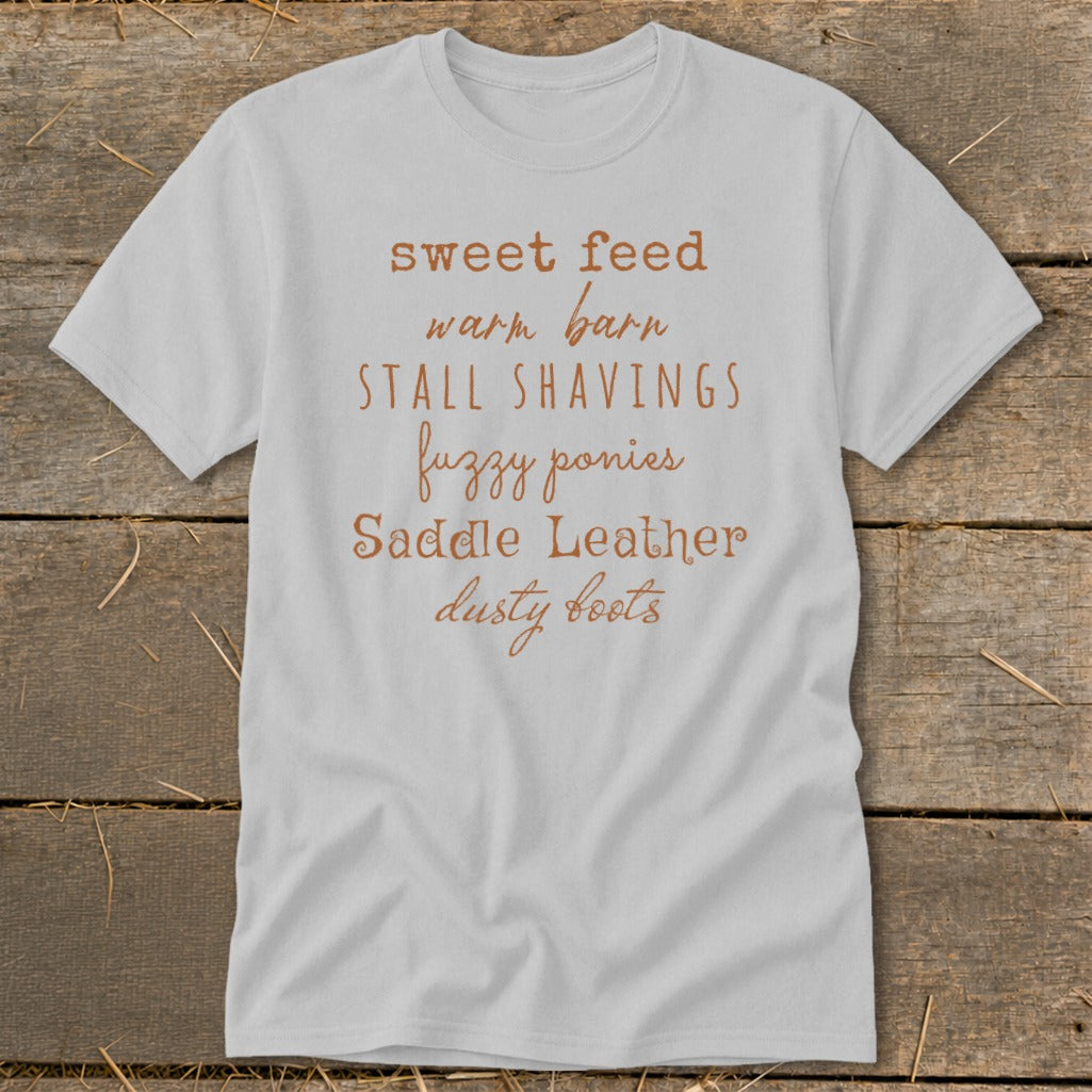 Light grey t-shirt with rustic text: "sweet feed, warm barn, stall shavings, fuzzy ponies, saddle leather, dusty boots".