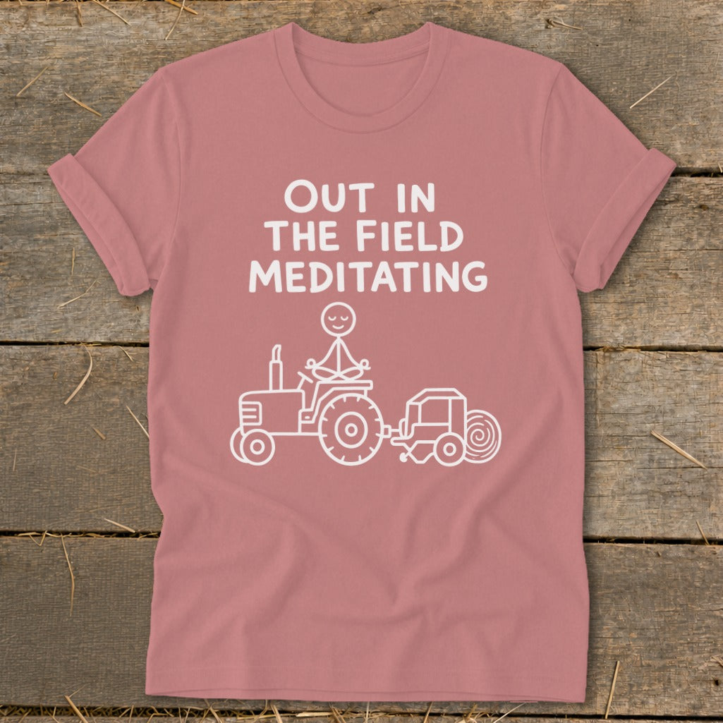 T-shirt with white text "OUT IN THE FIELD MEDITATING" and stick figure on tractor.