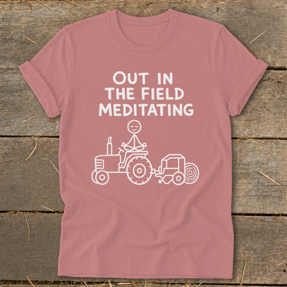 T-shirt with white text "OUT IN THE FIELD MEDITATING" and stick figure on tractor.