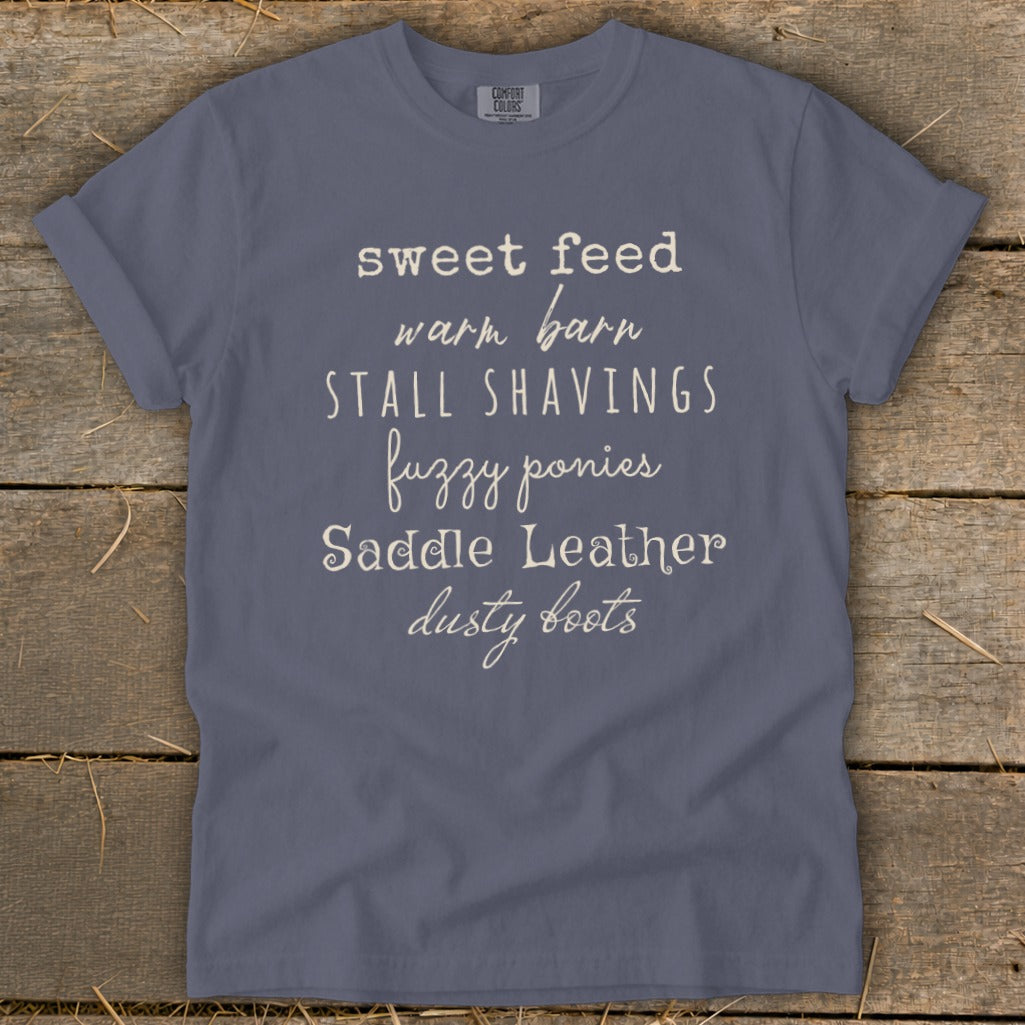 T-shirt with "sweet feed warm barn stall shavings fuzzy ponies saddle leather dusty boots" text.