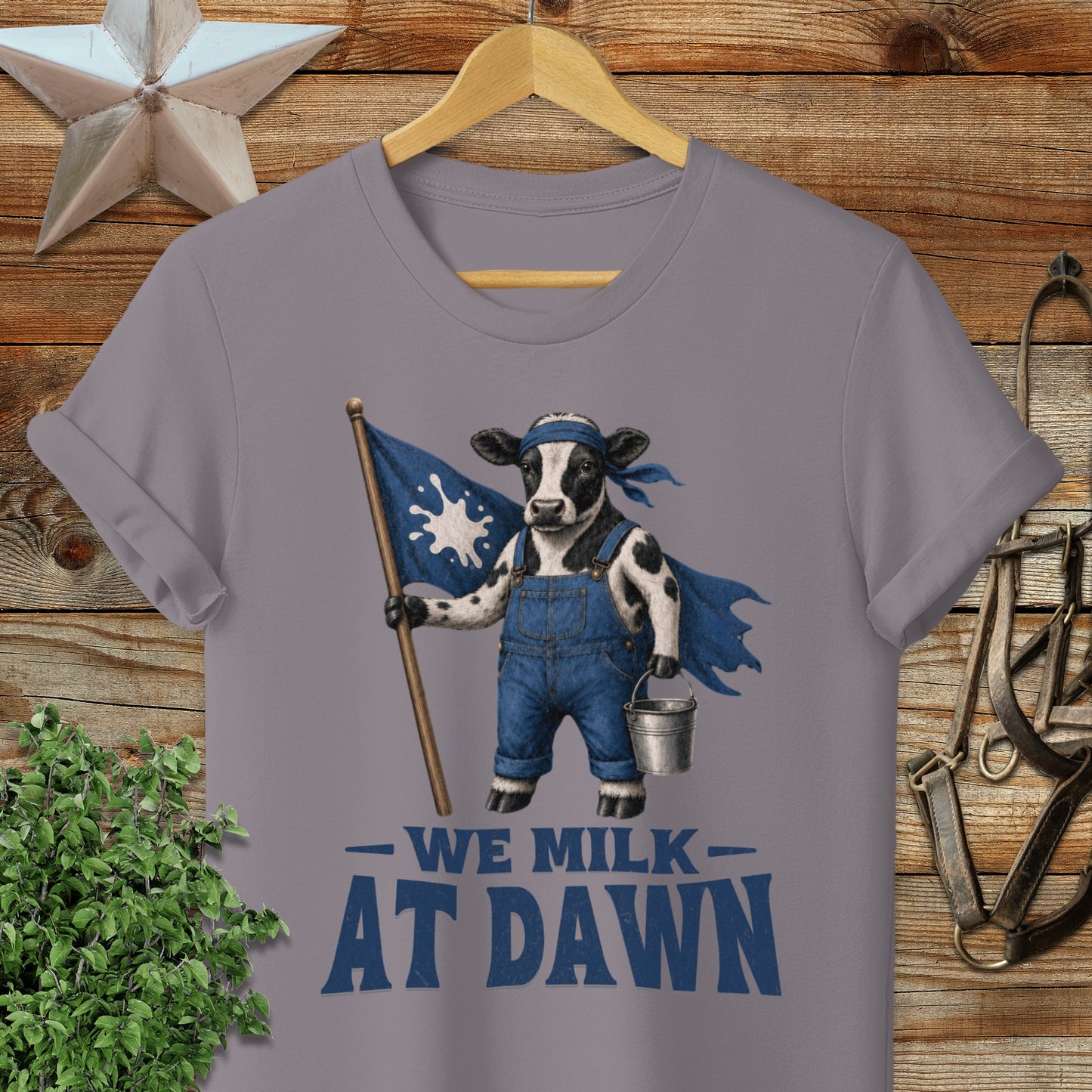 Cow wearing overalls and cape holding a flag and milk pail, text "WE MILK AT DAWN".
