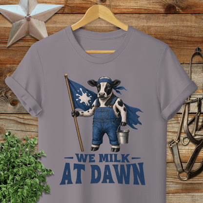 Cow wearing overalls and cape holding a flag and milk pail, text "WE MILK AT DAWN".