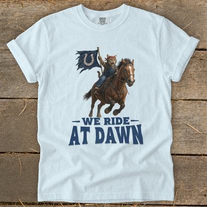White t-shirt with a cat riding a horse and holding a horseshoe flag, text reads "WE RIDE AT DAWN".