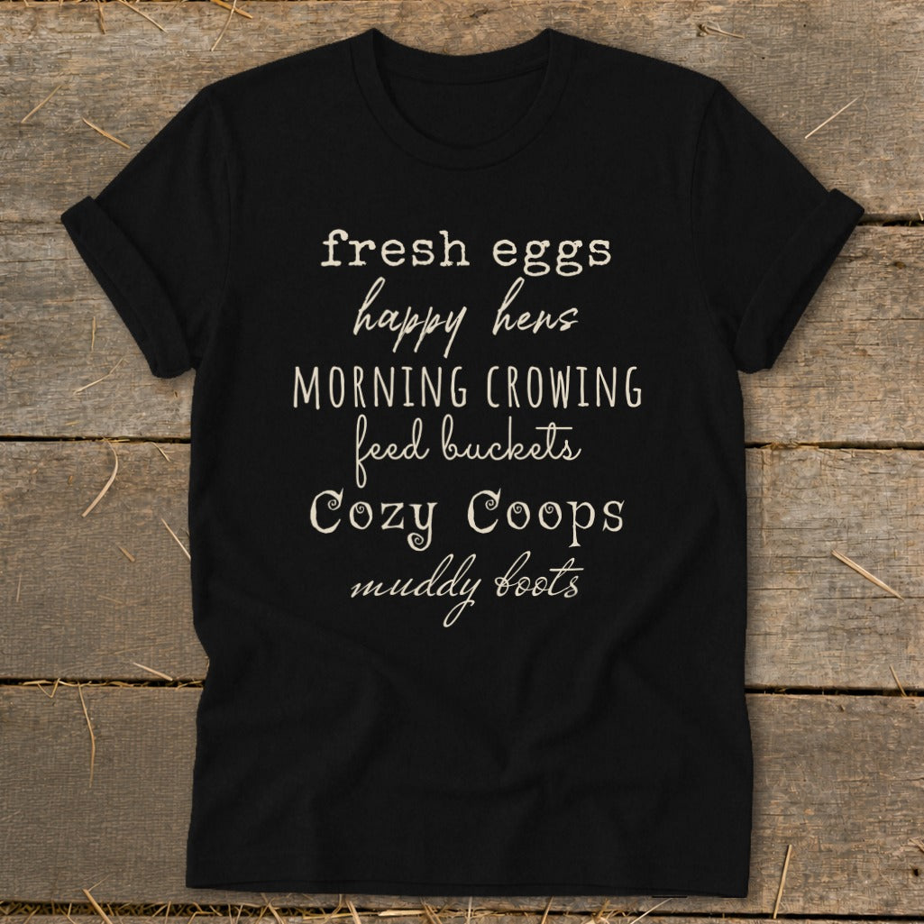 Black t-shirt with white text listing "fresh eggs, happy hens, morning crowing, feed buckets, Cozy Coops, muddy boots."