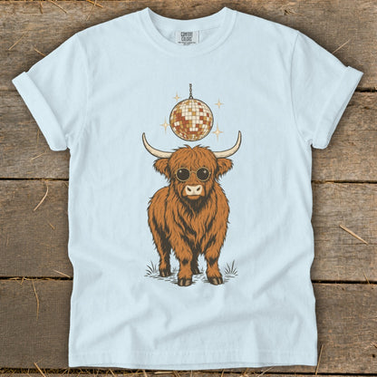 Highland cow wearing sunglasses under a disco ball on a light blue t-shirt.