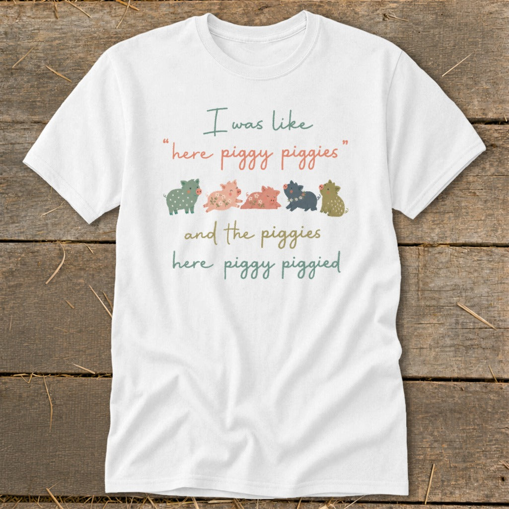 White t-shirt with text "I was like 'here piggy piggies' and the piggies here piggy piggied" and cartoon pigs.