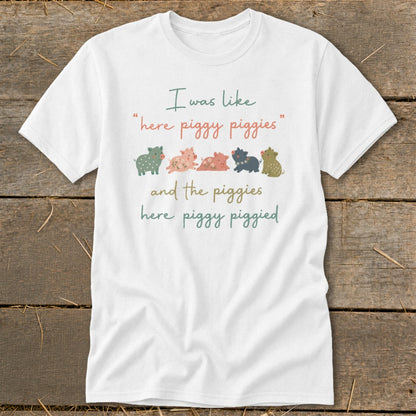 White t-shirt with text "I was like 'here piggy piggies' and the piggies here piggy piggied" and cartoon pigs.