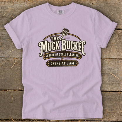 Light purple t-shirt with "The Muck Bucket School of Stall Cleaning Opens at 5 AM" graphic.