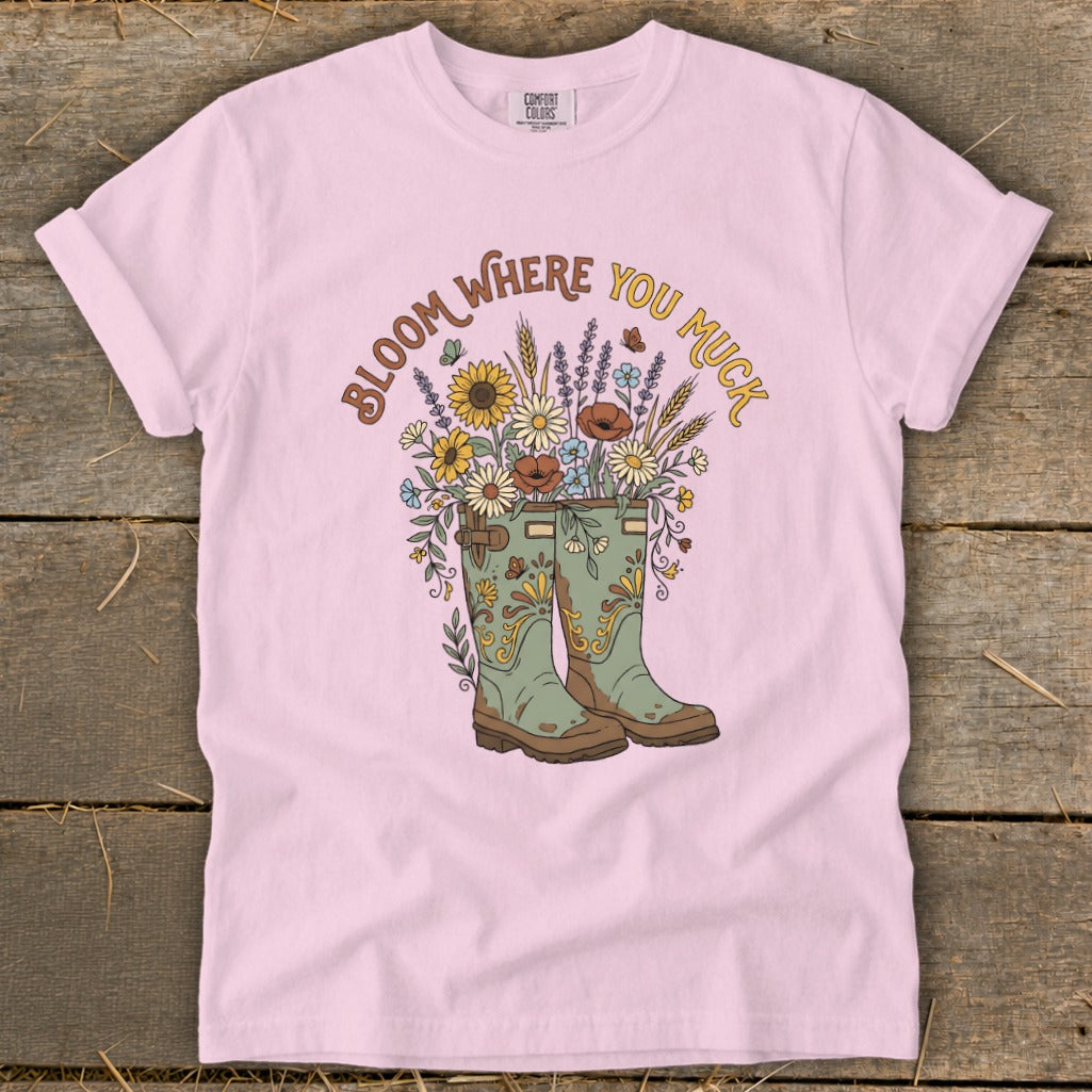 Pink t-shirt with "Bloom Where You Muck" text and floral bouquet in boots graphic.