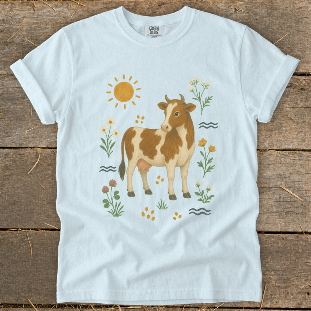 White t-shirt with a brown and white cow illustration surrounded by flowers and a sun.