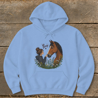 Light blue hoodie with graphic of a girl booping a horse in a field of flowers.