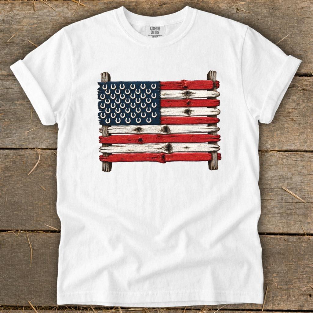 A white t-shirt featuring a rustic American flag made of weathered wooden planks and horseshoes.