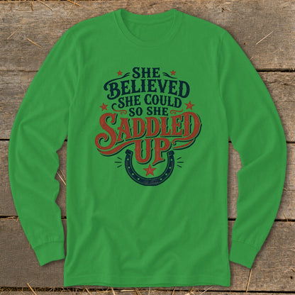 Green long-sleeve shirt with "She believed she could so she saddled up" text.