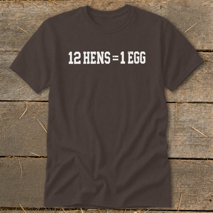 Dark brown short-sleeve t-shirt with white distressed text reading 12 HENS = 1 EGG, laid flat on a rustic wooden surface.