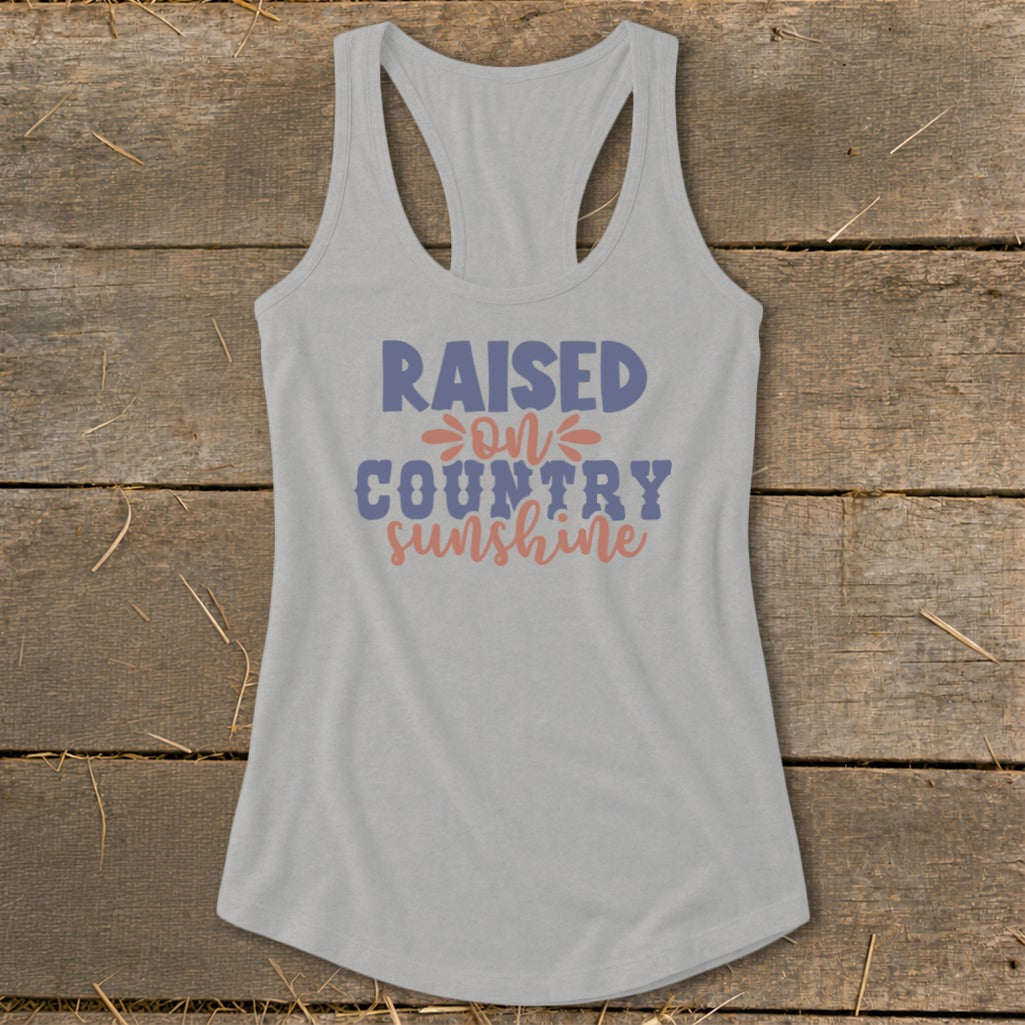 Grey racerback tank top with "Raised on Country Sunshine" text in blue and coral.