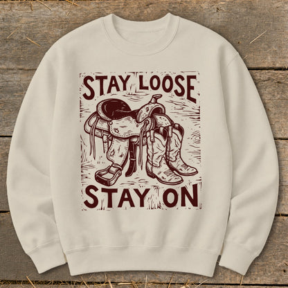 Cream sweatshirt with graphic of saddle and boots and text "Stay Loose Stay On."