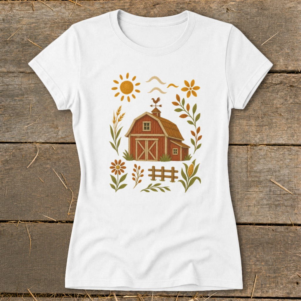 White t-shirt with a rustic farm scene featuring a red barn, sun, flowers, and fence.