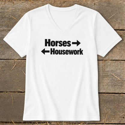 A white V-neck t-shirt with black text that reads Horses with a right arrow above Housework with a left arrow, laid flat on a rustic wooden background.