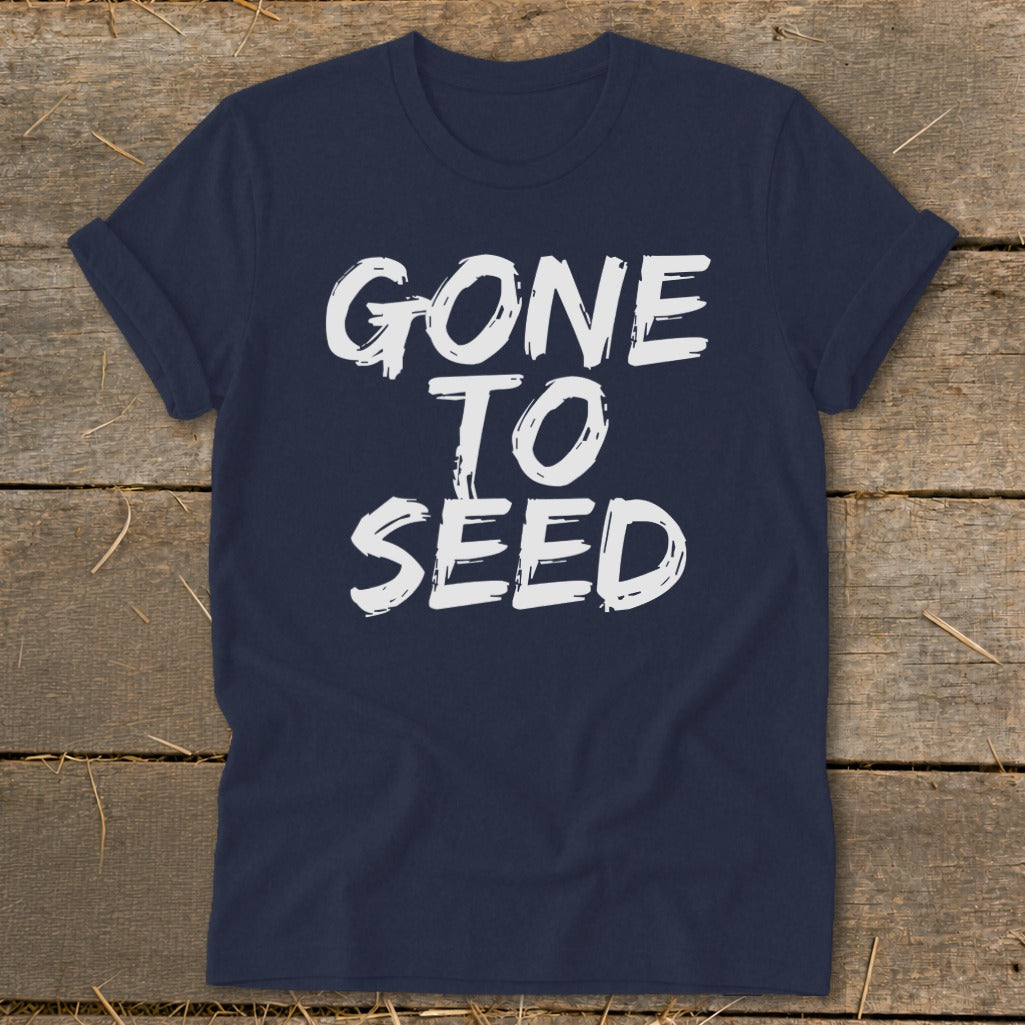 Navy t-shirt with white text "GONE TO SEED" on a wooden background.