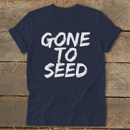 Navy t-shirt with white text "GONE TO SEED" on a wooden background.