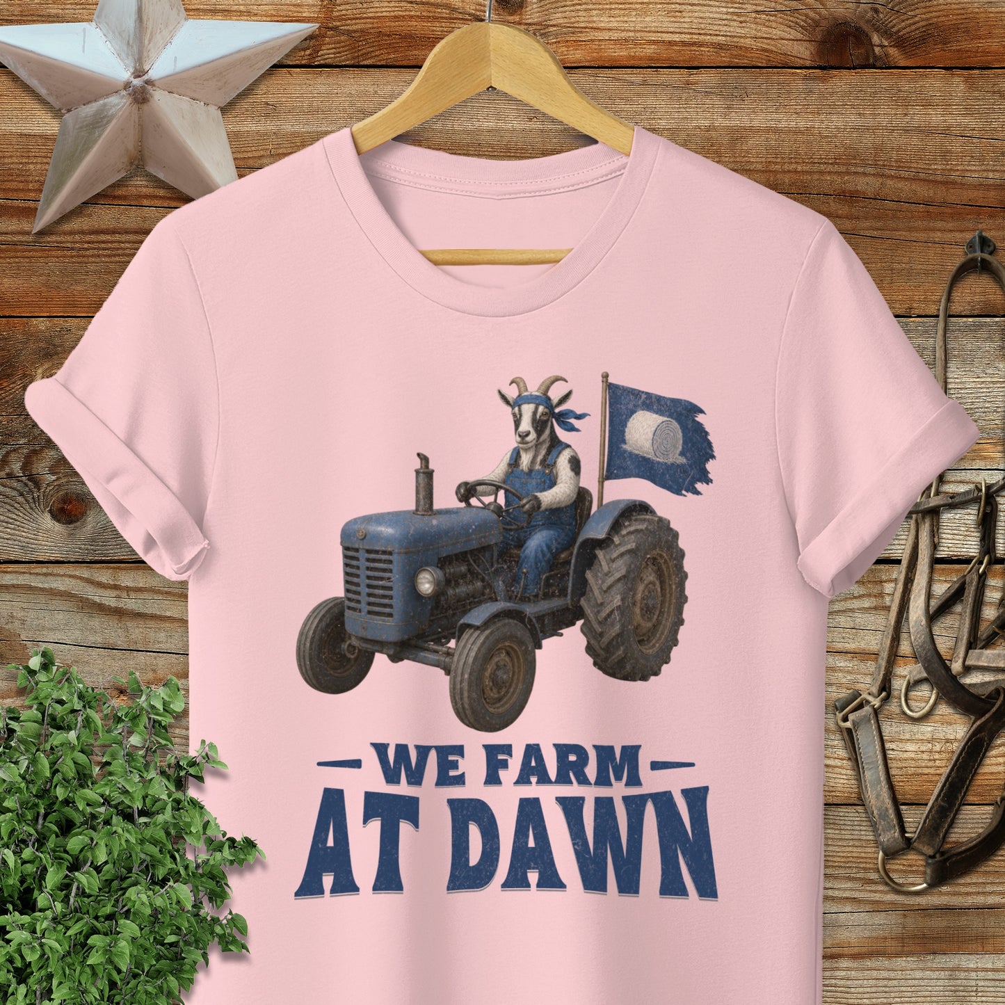 Pink t-shirt with a cartoon goat driving a blue tractor, holding a flag.