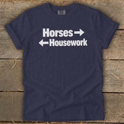 A navy blue t-shirt with white text that reads Horses with a right arrow and Housework with a left arrow.