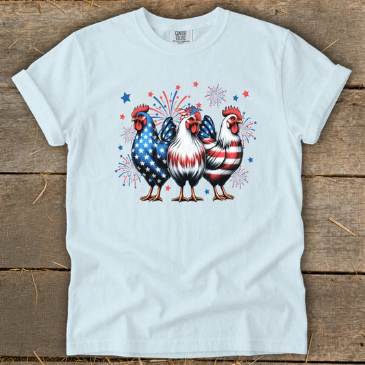 Three patriotic roosters with fireworks and stars on a light blue t-shirt.