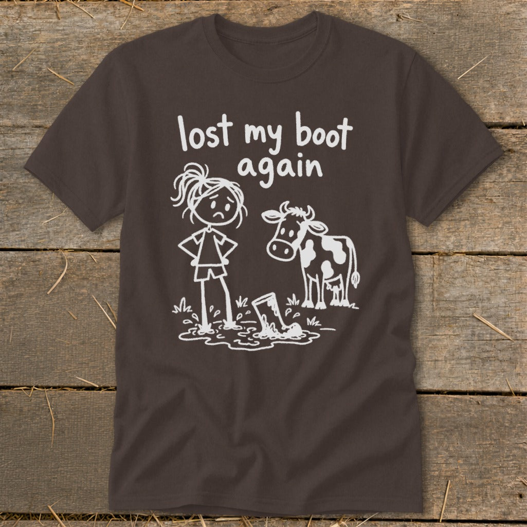 A dark brown t-shirt featuring a white line drawing of a sad girl and a cow standing near a boot stuck in mud, with the text "lost my boot again".