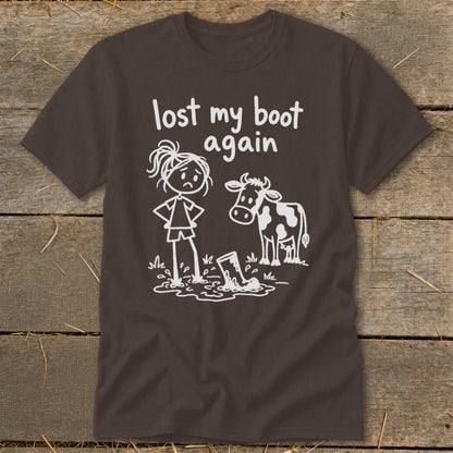 A dark brown t-shirt featuring a white line drawing of a sad girl and a cow standing near a boot stuck in mud, with the text "lost my boot again".