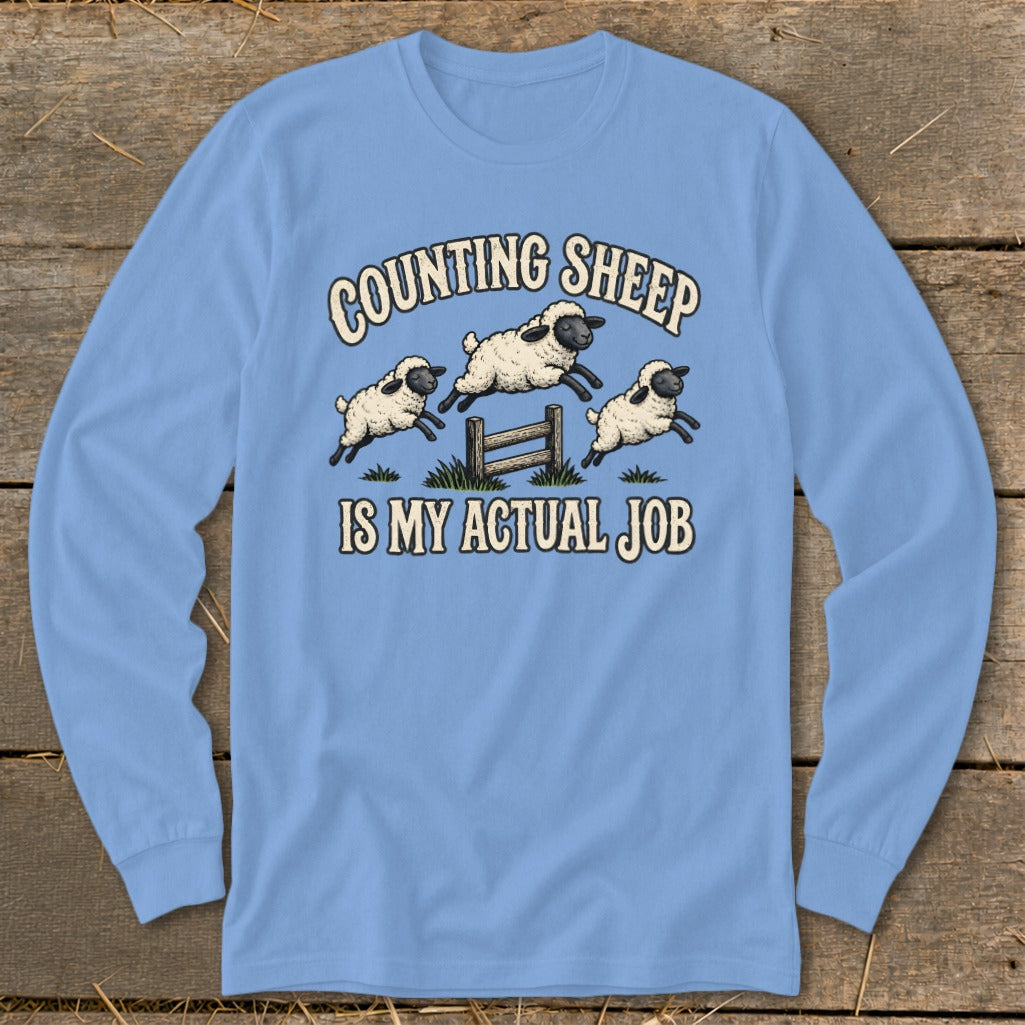 Light blue long-sleeve shirt with sheep jumping over a fence and text "COUNTING SHEEP IS MY ACTUAL JOB".