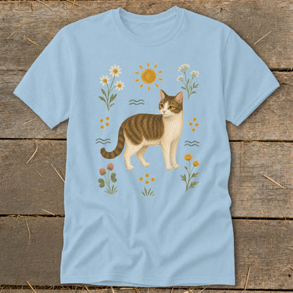 Light blue t-shirt with a tabby cat surrounded by flowers and sun.