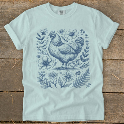 Light blue t-shirt with a blue sketch of a chicken surrounded by flowers and foliage.