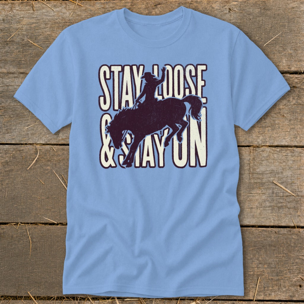 Light blue t-shirt with distressed graphic of a cowboy on a bucking horse and text "STAY LOOSE & STAY ON".