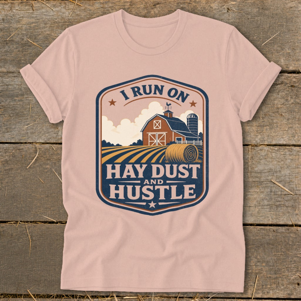 Pink t-shirt featuring a farm scene graphic with text "I RUN ON HAY DUST AND HUSTLE".
